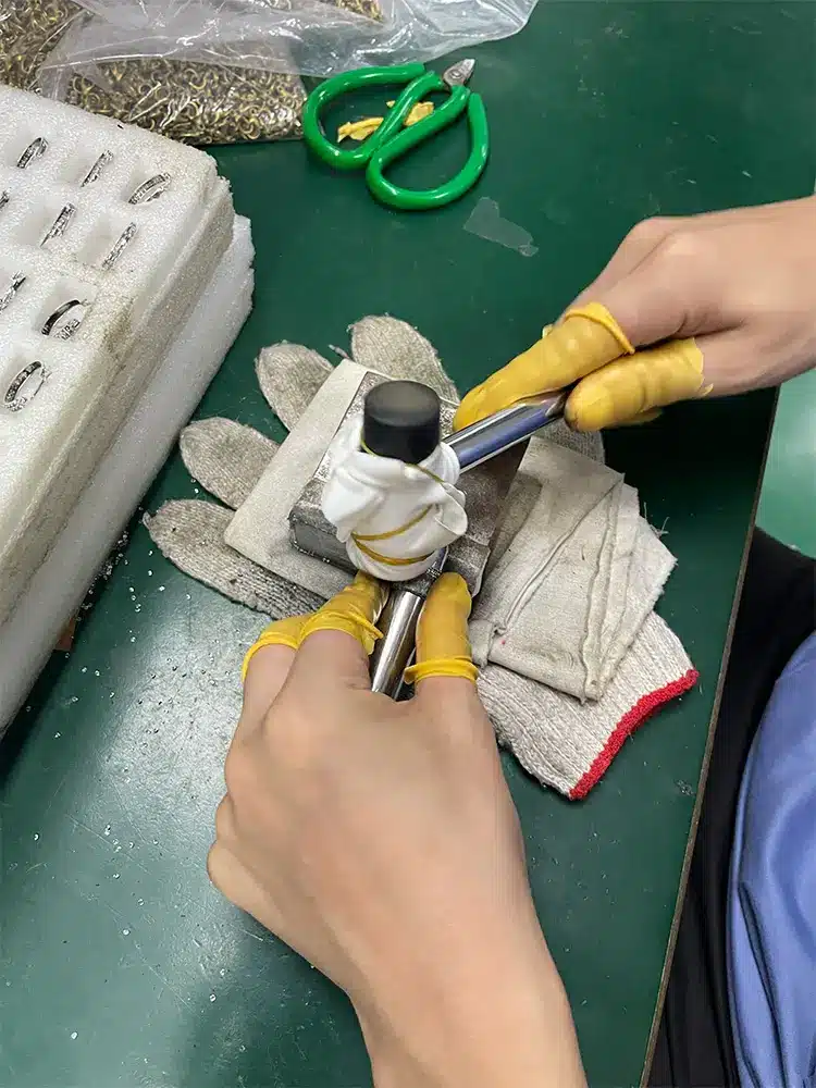 Hands holding pliers and a small jewelry component on a workbench