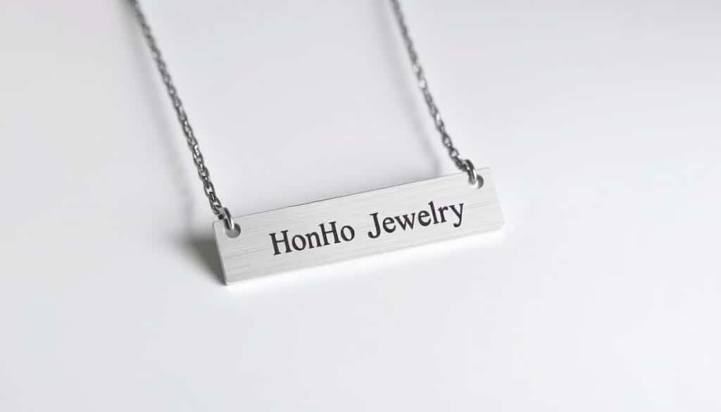 A custom stainless steel necklace with a sleek, modern design. The focal point is a rectangular name bar pendant in a brushed finish, with the brand name "HonHo Jewelry" engraved in a clean, sans-serif font. The necklace chain has a minimalist cable link style, also in stainless steel, creating a harmonious, high-quality look. Soft, directional lighting highlights the metallic sheen and showcases the piece's craftsmanship. The necklace is photographed against a plain, white background, allowing the product to be the central focus, emphasizing its elegant simplicity and versatility.