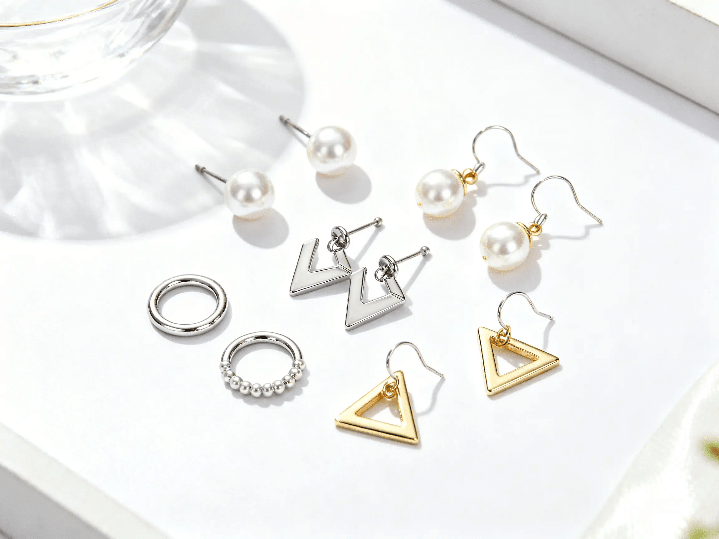 An assortment of silver-colored and gold-colored earrings on a white surface.