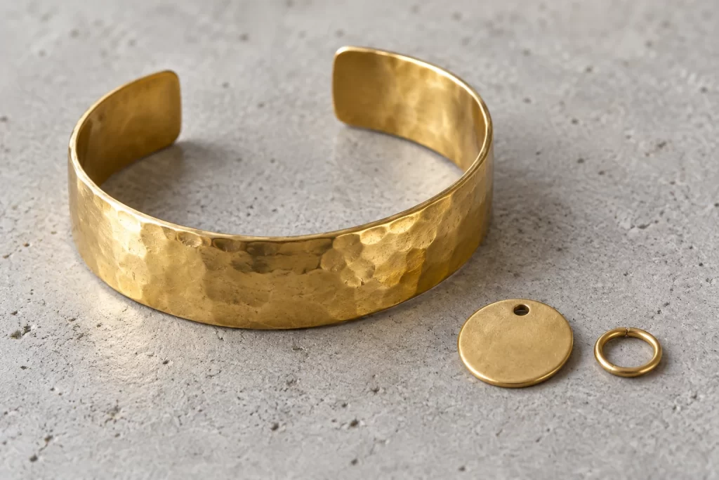Brass Jewelry: Material, Finishes, Styles and Trade-Offs 1 Hammered brass-colored cuff beside a smooth disk pendant